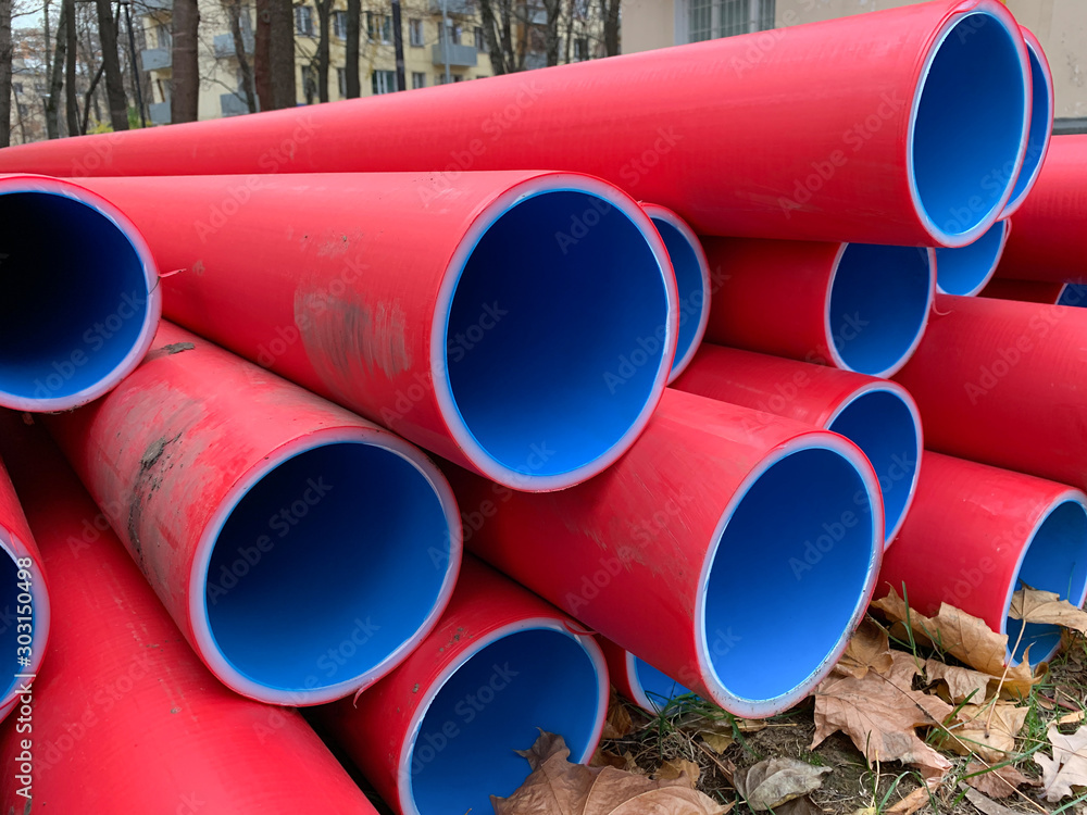 Many stacked red and blue pvc plastic plumbing tubes pipes lying on the ground outdoors