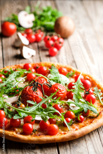Traditional italian pizza with cherry tomatoes on a wooden shovel on a dark background.