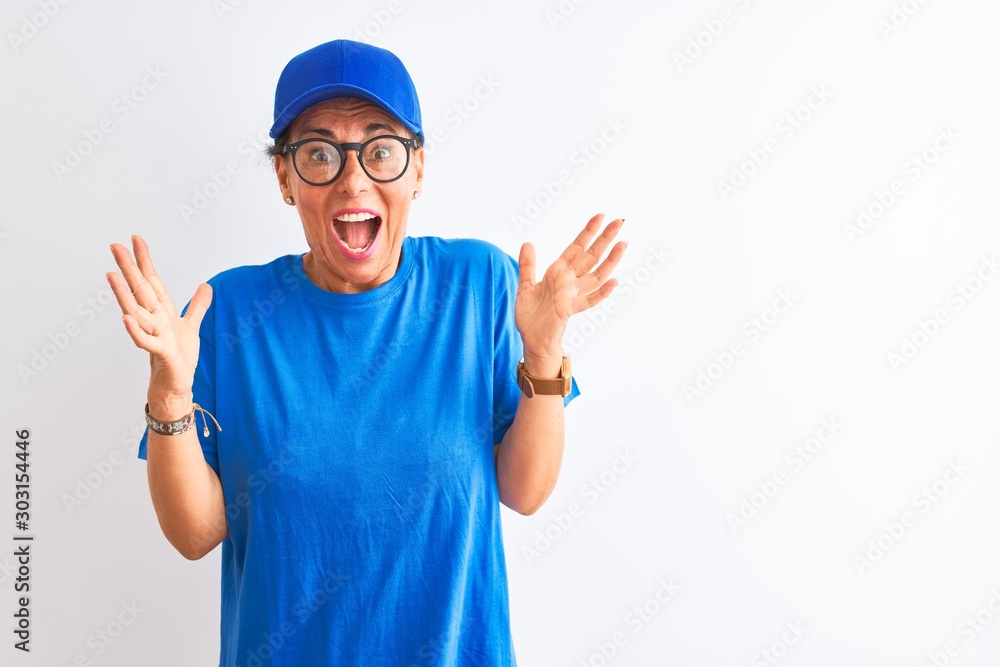 Senior deliverywoman wearing cap and glasses standing over isolated white background celebrating crazy and amazed for success with arms raised and open eyes screaming excited. Winner concept