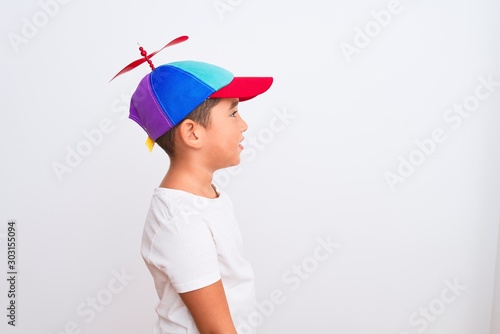 Beautiful kid boy wearing fanny colorful cap with propeller over isolated white background looking to side, relax profile pose with natural face with confident smile.