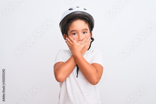 Beautiful kid boy wearing bike security helmet standing over isolated white background shocked covering mouth with hands for mistake. Secret concept. © Krakenimages.com