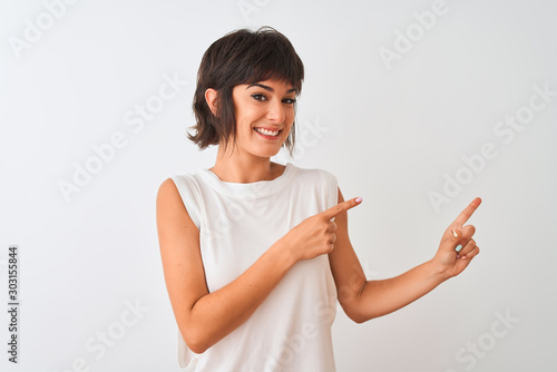 Young beautiful woman wearing casual t-shirt standing over isolated white background smiling and looking at the camera pointing with two hands and fingers to the side.