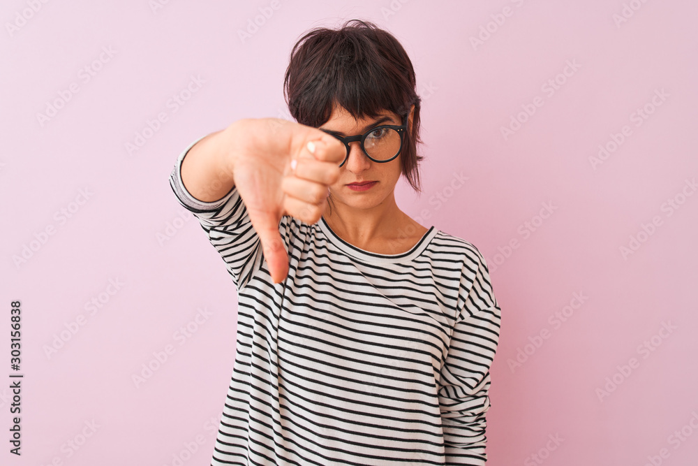 Young beautiful woman wearing striped t-shirt and glasses over isolated pink background looking unhappy and angry showing rejection and negative with thumbs down gesture. Bad expression. Young beautiful woman wearing striped t-shirt and glasses over isolated pink background looking unhappy and angry showing rejection and negative with thumbs down gesture. Bad expression.