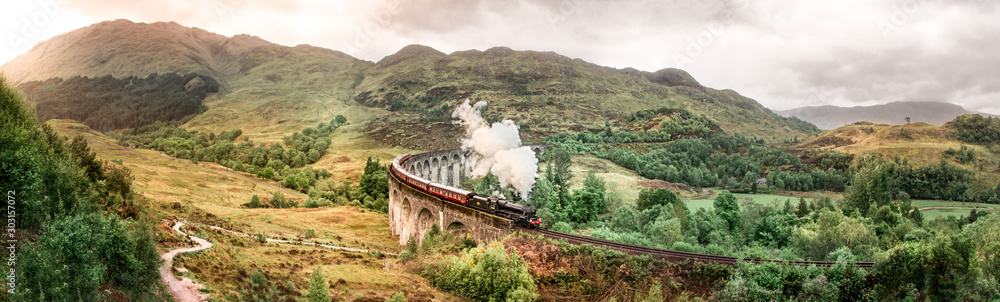 Glenfinnan Railway Viaduct with Jacobite steam train passing over. Harry Potter famous Glenfinnan viaduct, Scotland in cloudy weather with steam train. 