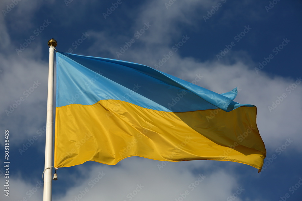 flag of ukraine waves on white flagpole against blue sky with nice white clouds flag of ukraine waves on white flagpole against blue sky with nice white clouds