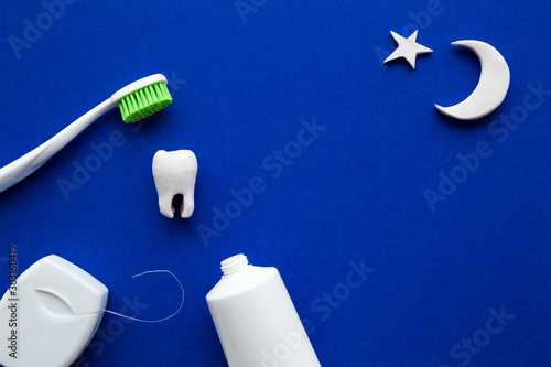 Toothbrush with green bristles, white tube of toothpaste, dental floss on dark blue background. Moon and star shape. Healthy teeth. Evening hygiene concept. Top down view.