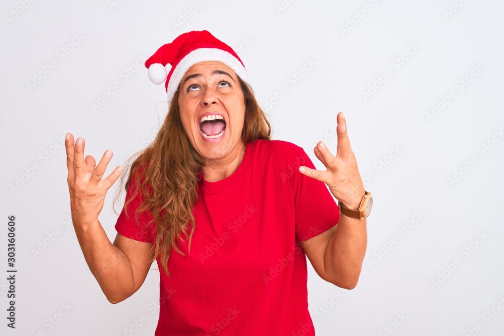 Middle age mature woman wearing christmas hat over isolated background crazy and mad shouting and yelling with aggressive expression and arms raised. Frustration concept. Middle age mature woman wearing christmas hat over isolated background crazy and mad shouting and yelling with aggressive expression and arms raised. Frustration concept.