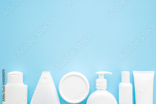 Different white toiletries on light pastel blue table. Care about face, hands, legs and body skin. Women beauty products. Empty place for text or logo. Flat lay. Top down view. photo