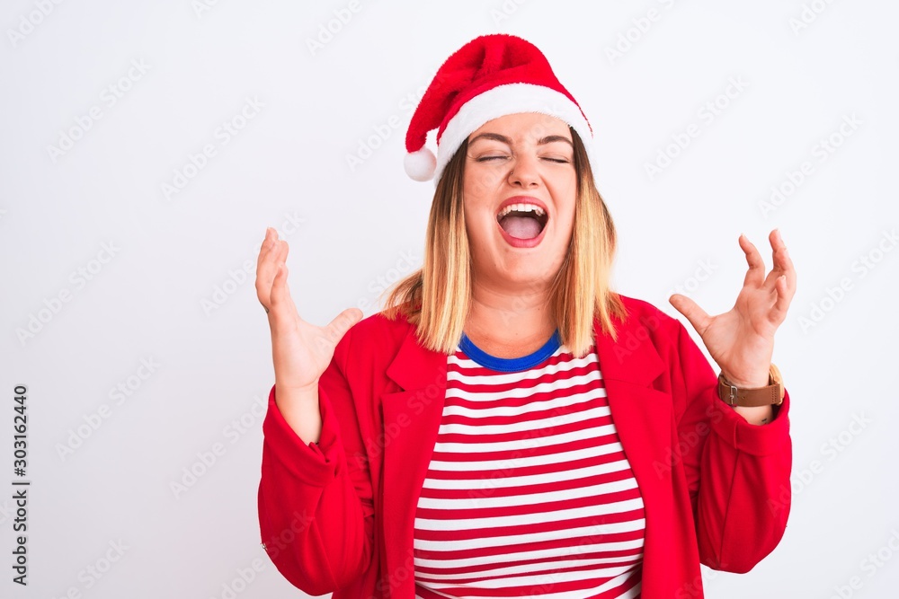 Young beautiful woman wearing Christmas Santa hat over isolated white background celebrating mad and crazy for success with arms raised and closed eyes screaming excited. Winner concept Young beautiful woman wearing Christmas Santa hat over isolated white background celebrating mad and crazy for success with arms raised and closed eyes screaming excited. Winner concept