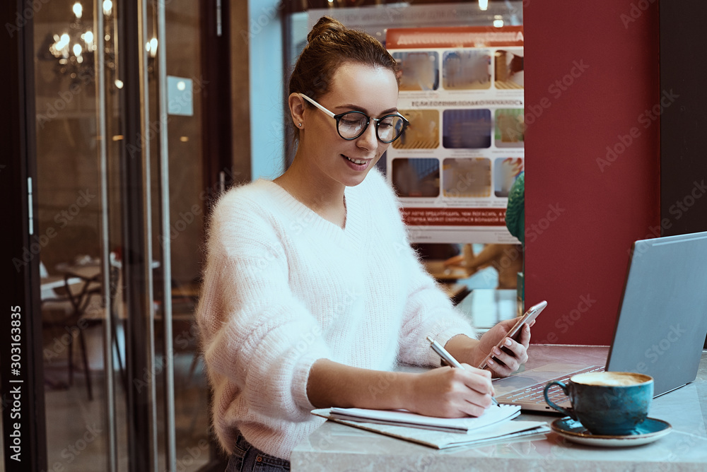 Woman entrepreneur working from cafe and talking on mobile phone with headphones