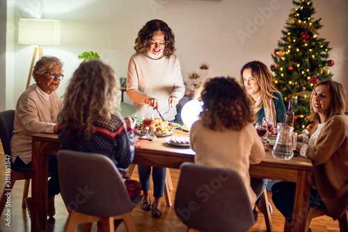 Beautiful group of women smiling happy and confident. Carving roasted turkey celebrating christmas at home