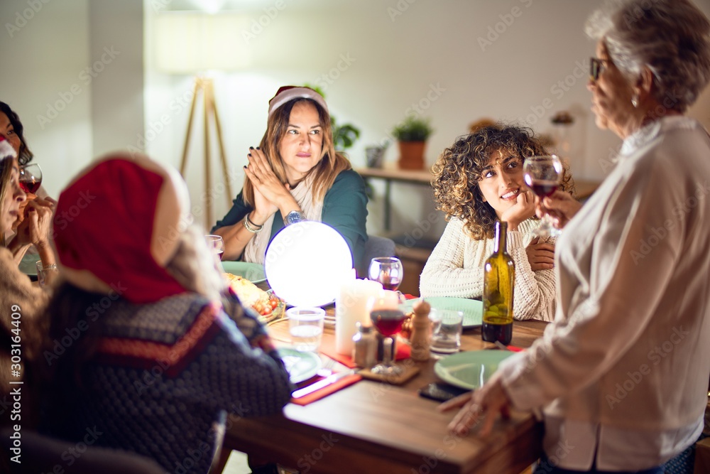 Beautiful group of women smiling happy and confident. On of them holding cup of wine speaking speech celebrating christmas at home