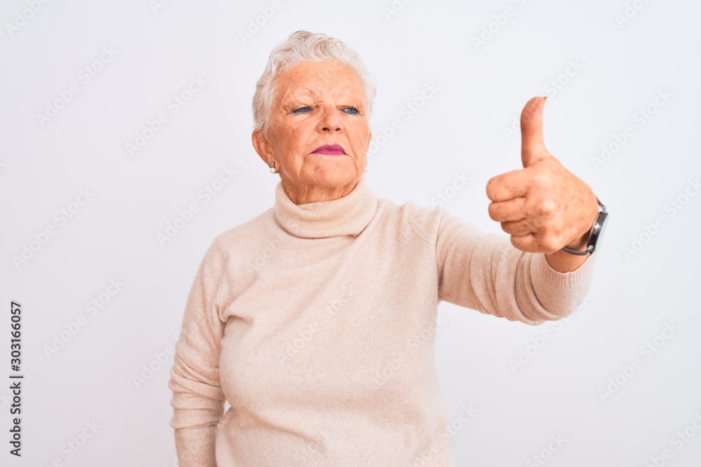 Senior grey-haired woman wearing turtleneck sweater standing over isolated white background Looking proud, smiling doing thumbs up gesture to the side Senior grey-haired woman wearing turtleneck sweater standing over isolated white background Looking proud, smiling doing thumbs up gesture to the side