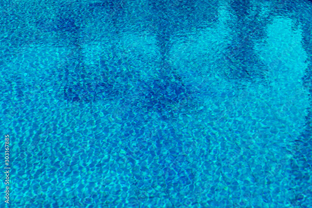 swimming pool water with palm trees and parasols reflected in it