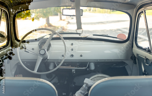 Interior of small white vintage car on the street. No people. White steering wheel.