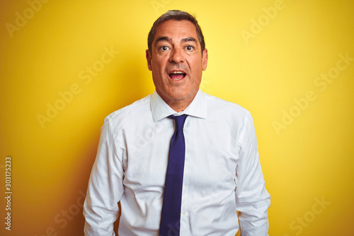Handsome middle age businessman standing over isolated yellow background afraid and shocked with surprise expression, fear and excited face.