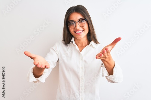 Young beautiful businesswoman wearing glasses standing over isolated white background smiling cheerful offering hands giving assistance and acceptance.