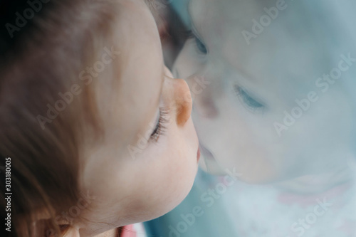 Foto A lonely sad little child looks out the window, leaning against the glass and reflecting in the glass