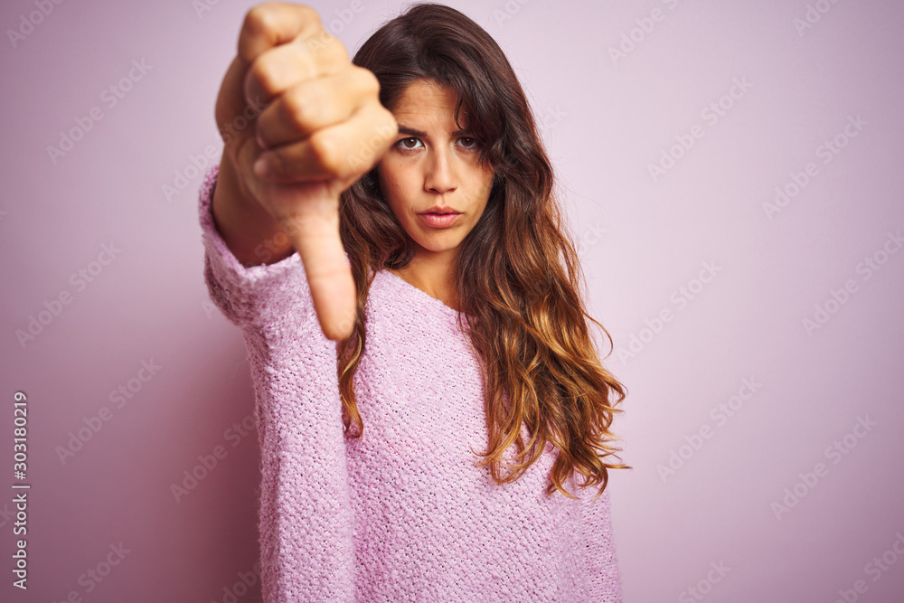 Young beautiful woman wearing sweater standing over pink isolated background looking unhappy and angry showing rejection and negative with thumbs down gesture. Bad expression. - obrazy, fototapety, plakaty 