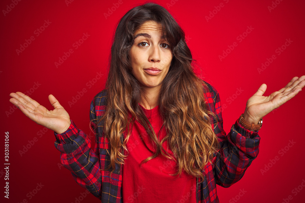 Young beautiful woman wearing casual jacket standing over red isolated background Surprised pointing with hand finger to the side, open mouth amazed expression. Young beautiful woman wearing casual jacket standing over red isolated background Surprised pointing with hand finger to the side, open mouth amazed expression.