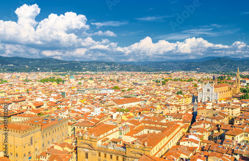 Top aerial panoramic view of Florence city historical centre, Basilica di Santa Croce di Firenze, buildings houses with orange red tiled roofs, hills range, blue sky white clouds, Tuscany, Italy