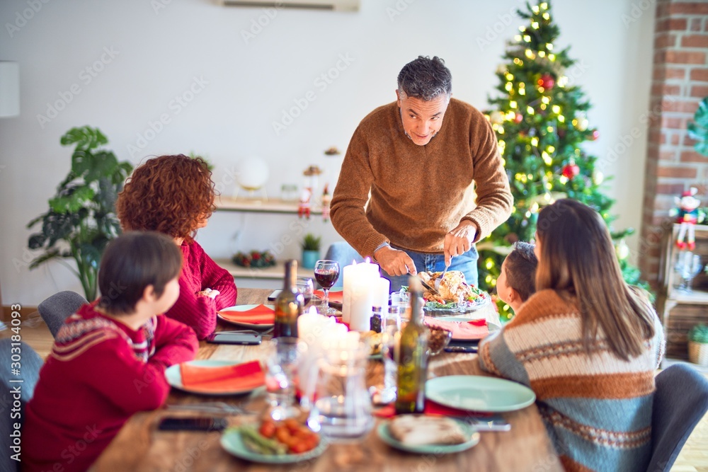 Beautiful family smiling happy and confident. One of them curving roasted turkey celebrating christmas at home