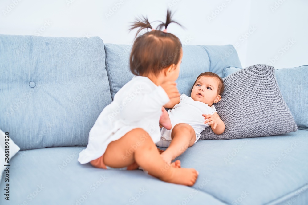 Beautiful infant happy girls playing together at home kindergarten sitting on the sofa Beautiful infant happy girls playing together at home kindergarten sitting on the sofa