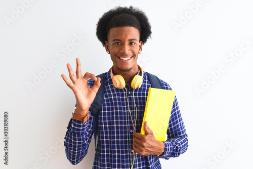 African american student man wearing headphones backpack over isolated white background doing ok sign with fingers, excellent symbol
