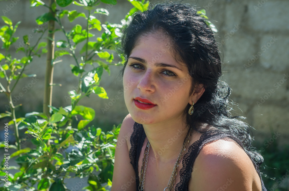 Cute Cuban girl with green bush background. White skin, green eyes and red lips look serious at camera Cute Cuban girl with green bush background. White skin, green eyes and red lips look serious at camera