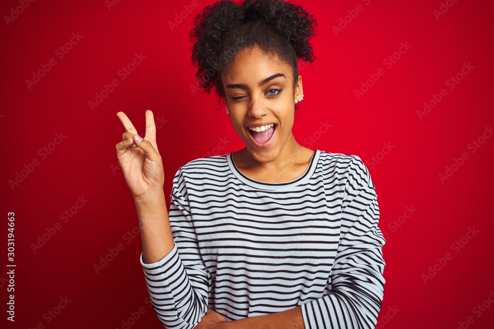 African american woman wearing navy striped t-shirt standing over isolated red background smiling with happy face winking at the camera doing victory sign. Number two. African american woman wearing navy striped t-shirt standing over isolated red background smiling with happy face winking at the camera doing victory sign. Number two.