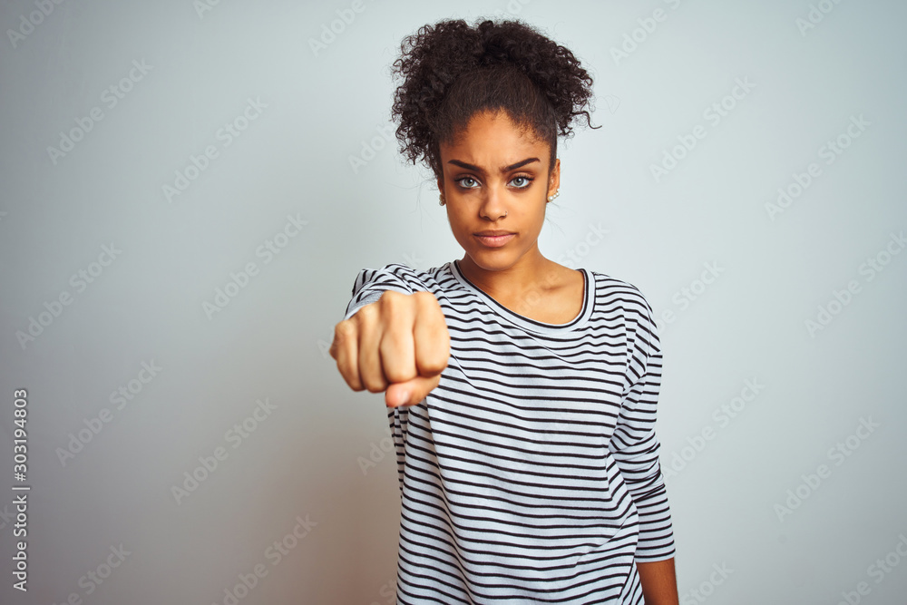 Fototapeta premium African american woman wearing navy striped t-shirt standing over isolated white background Punching fist to fight, aggressive and angry attack, threat and violence
