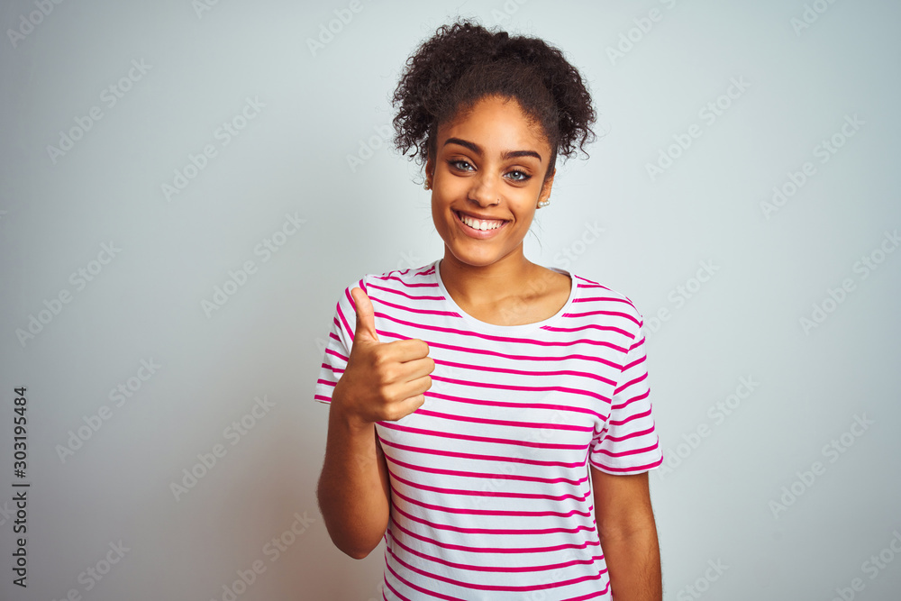 African american woman wearing casual pink striped t-shirt over isolated white background doing happy thumbs up gesture with hand. Approving expression looking at the camera with showing success. African american woman wearing casual pink striped t-shirt over isolated white background doing happy thumbs up gesture with hand. Approving expression looking at the camera with showing success.