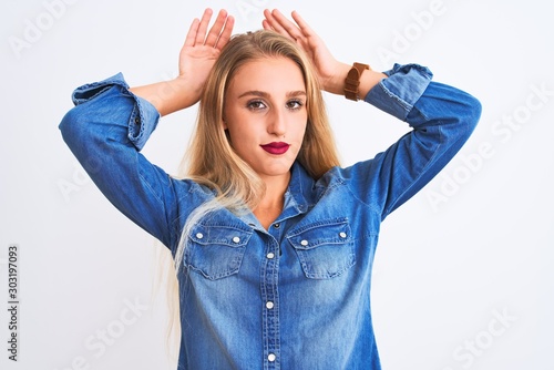 Young beautiful woman wearing casual denim shirt standing over isolated white background Doing bunny ears gesture with hands palms looking cynical and skeptical. Easter rabbit concept.