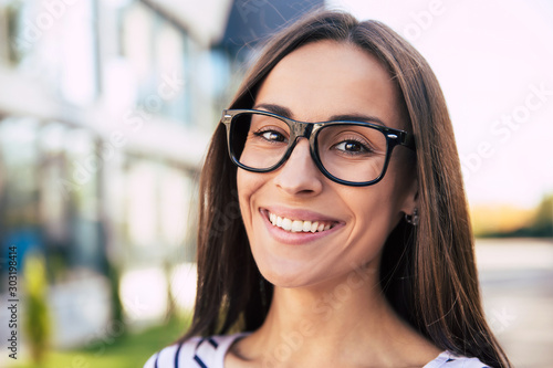 Fashionable student. Full-face portrait of a good-looking female student in glasses, who is smiling broadly while looking in the camera.