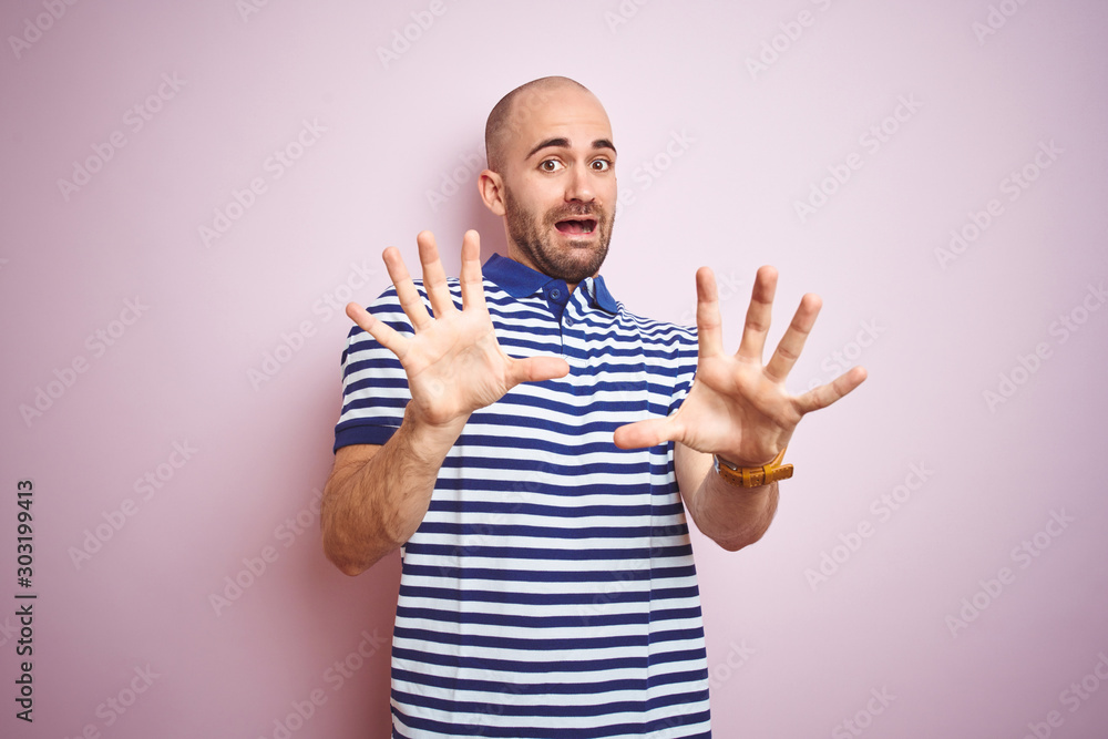 Fototapeta premium Young bald man with beard wearing casual striped blue t-shirt over pink isolated background afraid and terrified with fear expression stop gesture with hands, shouting in shock. Panic concept.