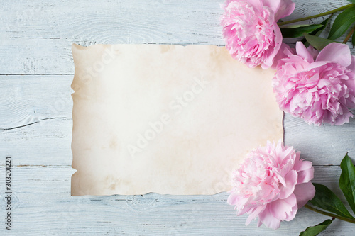 Pink peonies on a wooden background and a sheet of paper for congratulations, invitations
