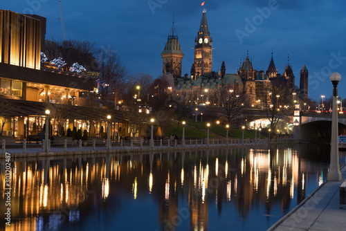 Nightscape of Ottawa's Parliament Hill and the reflections of the buildings in the Ottawa River. The lights have a golden hue and the Rideau River is still.