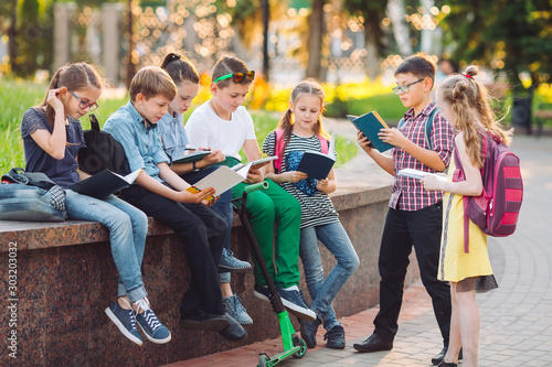 Happy Schoolmates Portrait. Schoolmates seating with books in a wooden bench in a city park and studying on sunny day.