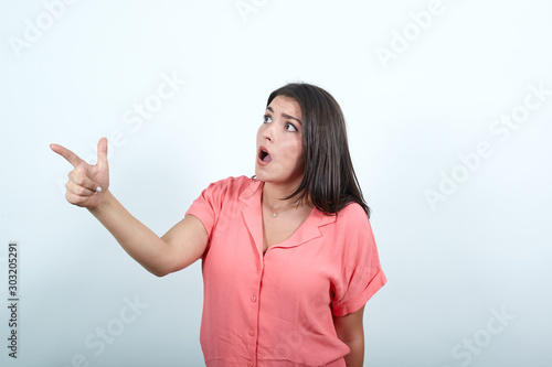 Young woman over isolated white wall pointing away. Lady points her index finger at an object or direction