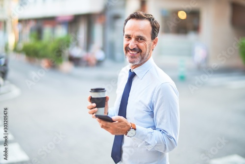 Middle age handsome businessman using smartphone drinking take away coffee smiling
