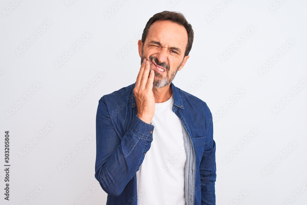 Middle age handsome man wearing blue denim shirt standing over isolated white background touching mouth with hand with painful expression because of toothache or dental illness on teeth Middle age handsome man wearing blue denim shirt standing over isolated white background touching mouth with hand with painful expression because of toothache or dental illness on teeth