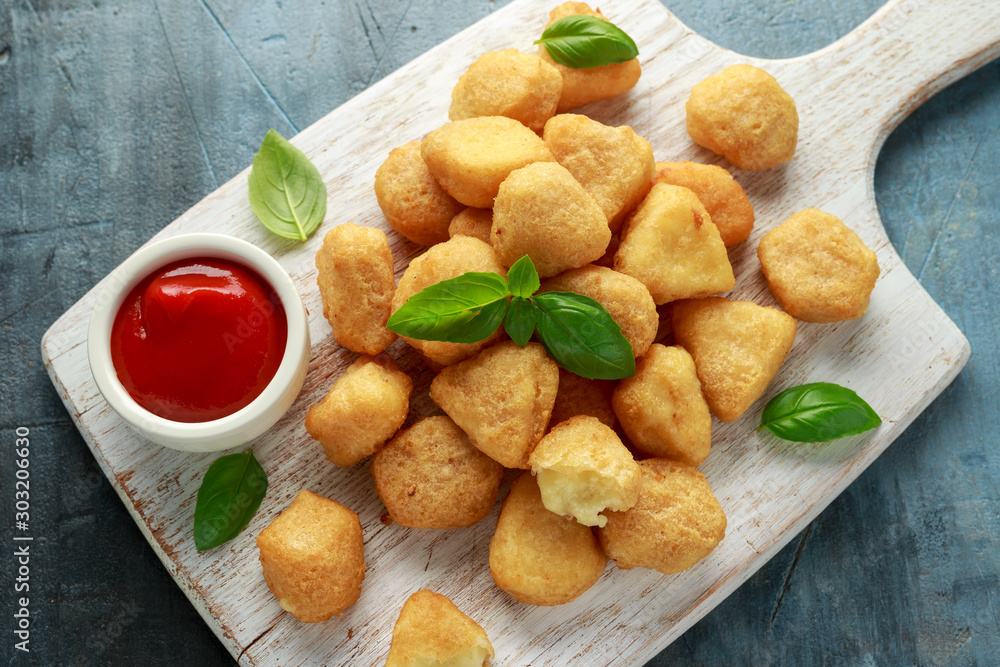 Fried mozzarella, cheddar cheese bites, balls with ketchup on white wooden board Fried mozzarella, cheddar cheese bites, balls with ketchup on white wooden board