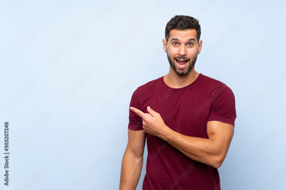 Handsome man over isolated blue background surprised and pointing side Handsome man over isolated blue background surprised and pointing side