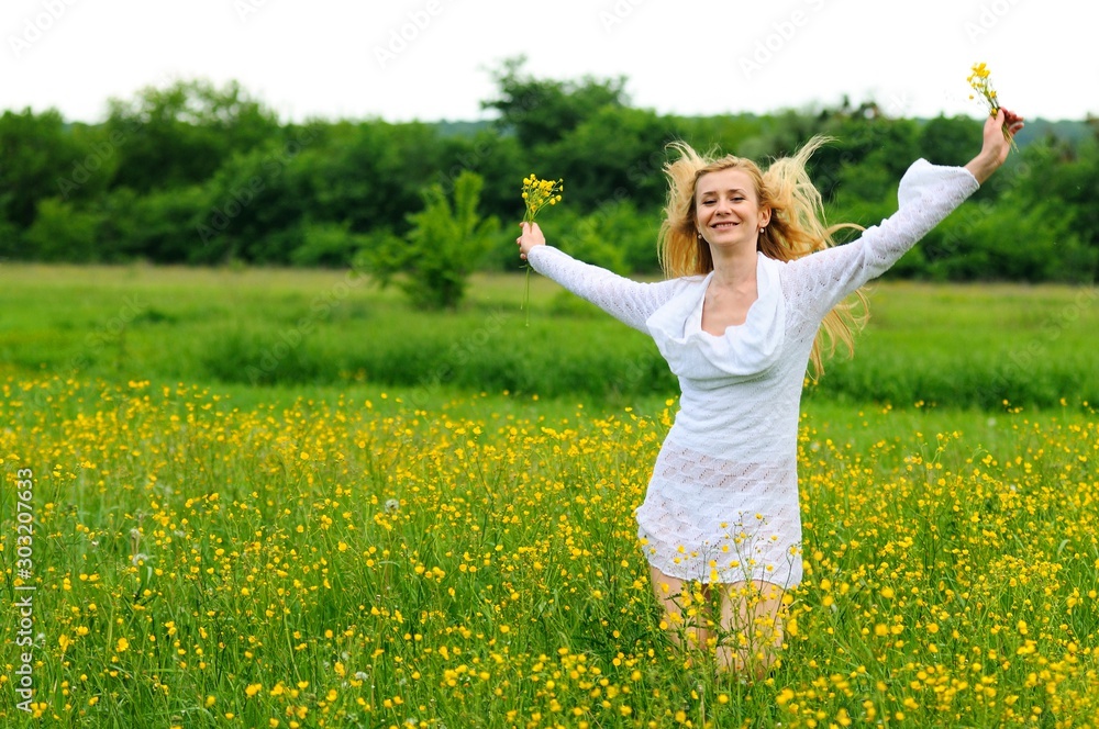 Naklejka premium Happy girl posing with hands up in a yellow flower field. Blonde young woman in a white lace dress