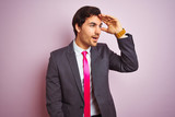 Young handsome businessman wearing suit and tie standing over isolated pink background very happy and smiling looking far away with hand over head. Searching concept.