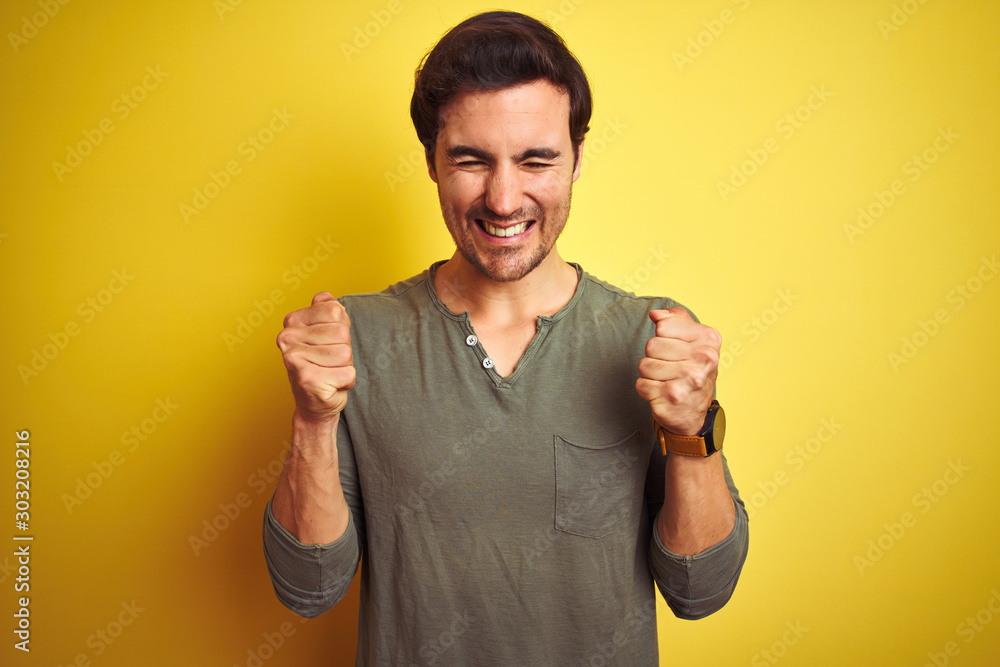 Fototapeta premium Young handsome man wearing casual t-shirt standing over isolated yellow background excited for success with arms raised and eyes closed celebrating victory smiling. Winner concept.