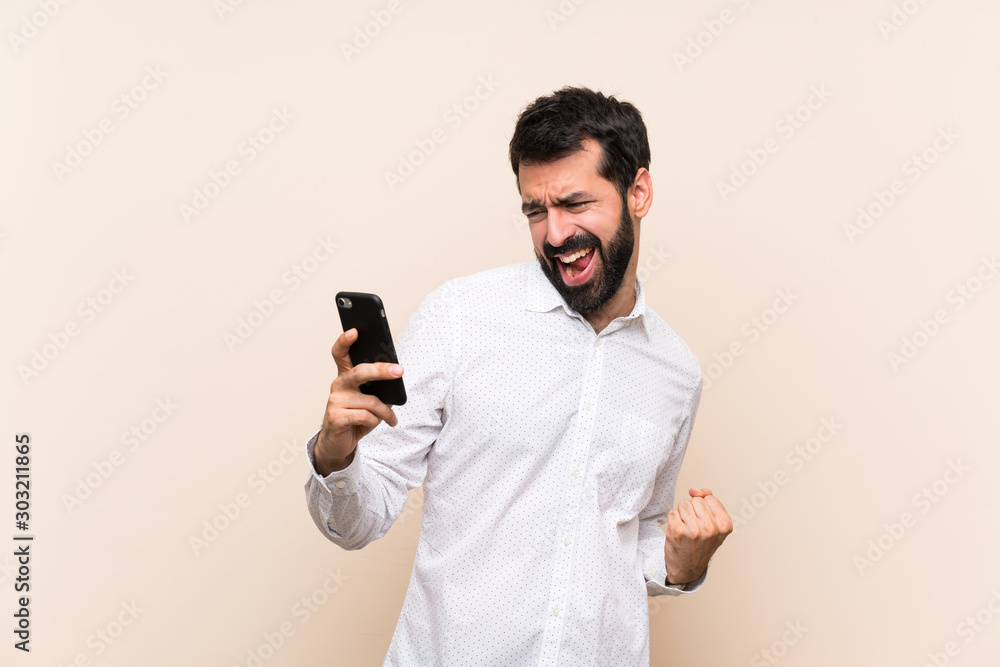 Young man with beard holding a mobile with phone in victory position Young man with beard holding a mobile with phone in victory position