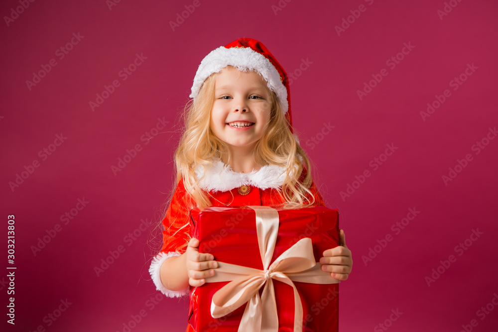 little blonde girl in Santa costume catches snow is holding a large red gift box in her hands little blonde girl in Santa costume catches snow is holding a large red gift box in her hands