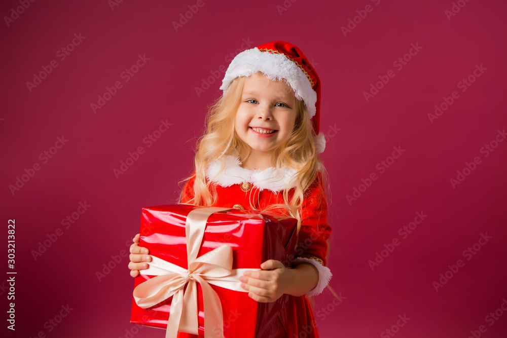 little blonde girl in Santa costume catches snow is holding a large red gift box in her hands little blonde girl in Santa costume catches snow is holding a large red gift box in her hands