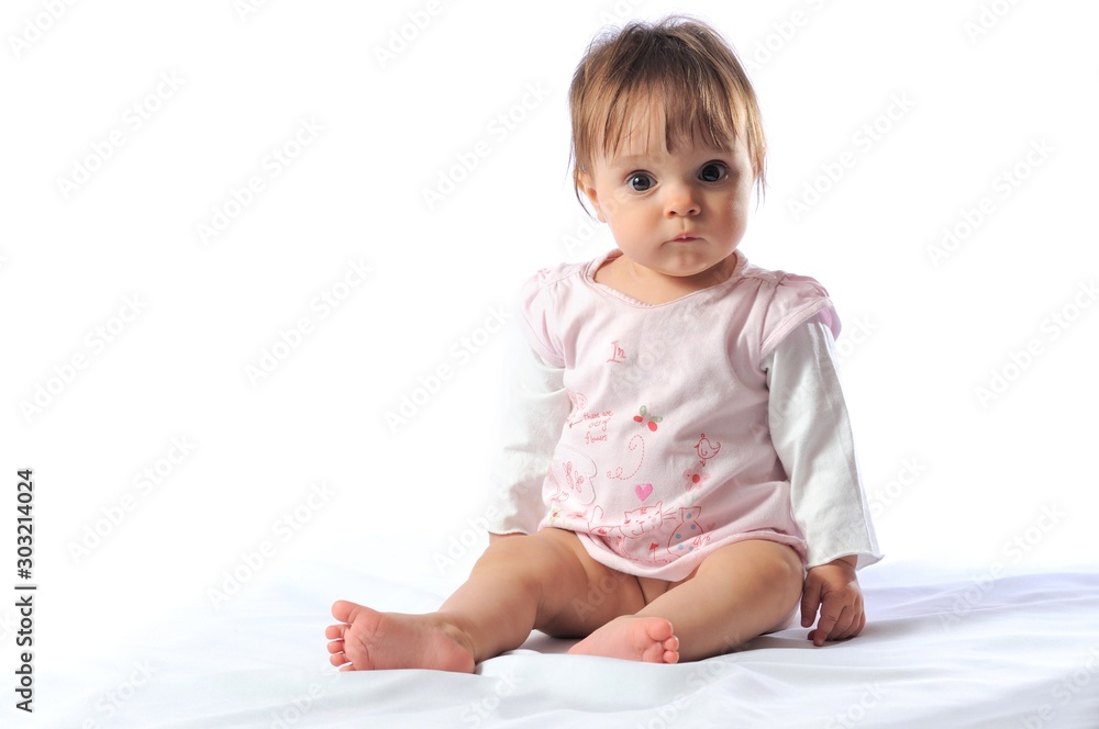 Happy beautiful smiling one year baby sitting with bib portrait. Childhood. Cute little girl on light background Happy beautiful smiling one year baby sitting with bib portrait. Childhood. Cute little girl on light background